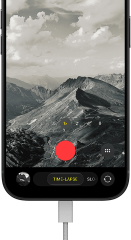 iPhone 18 Pro, Vorderseite, das Display zeigt eine Berglandschaft, mit der Kamera Modus Überlagerung im Zeitraffer Modus, mit dem Netzkabel am Ladeanschluss