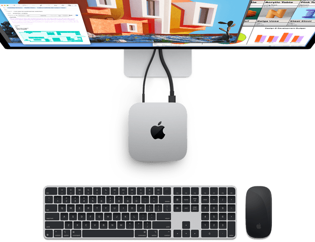 Draufsicht auf den Mac mini in Silber mit Apple Logo, angeschlossen an einen Monitor und neben einem kabellosen Magic Keyboard und einer kabellosen Magic Mouse